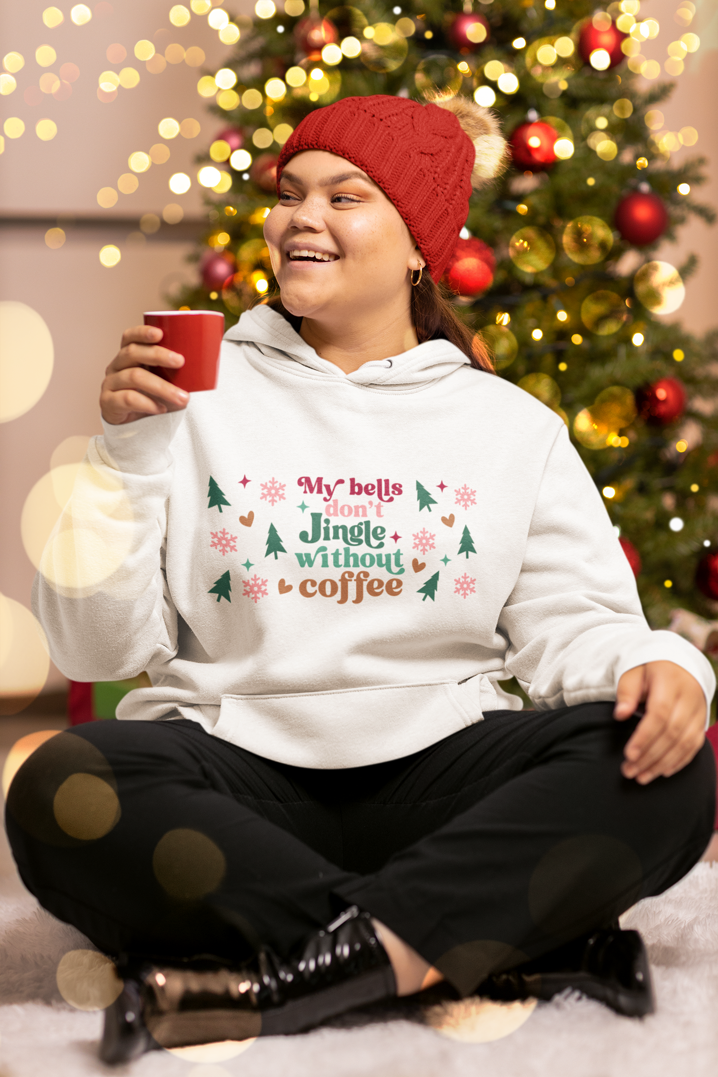White women’s hoodie with colorful festive print and the phrase “My bells don’t jingle without coffee”